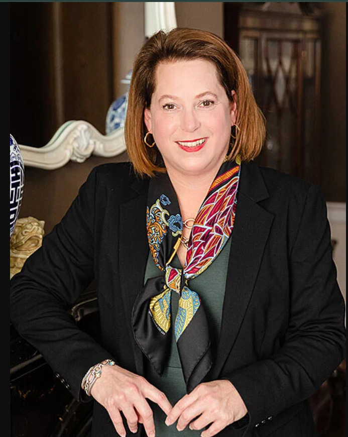 Professional headshot of Zandoria Lubbert in business attire - black blazer with colorful patterned scarf, professional makeup and styling, elegant office background
